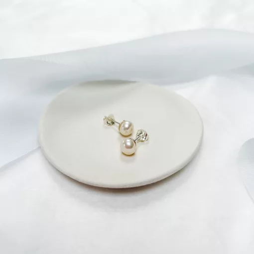 Traditional classic freshwater pearl stud earrings in silver set on a small ivory dish with blue ribbon
