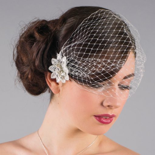 Woman with dark hair models a bridal side bun with bandeau bridal birdcage veil, on a grey background