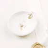 dainty leaf pearl drop bridal earrings set on a small dish with plain background and ivory silk ribbon