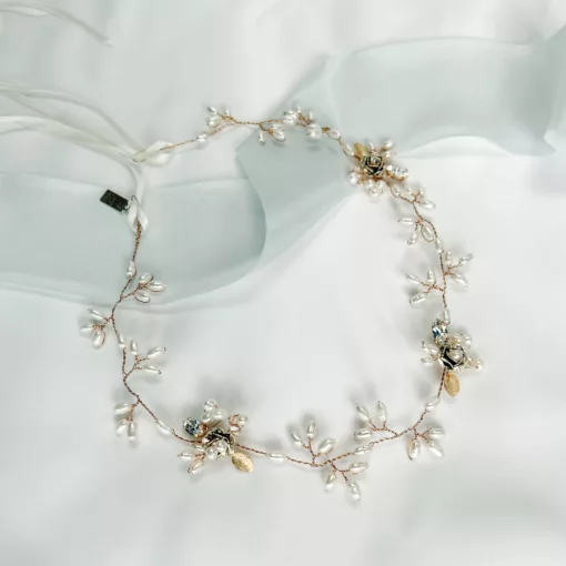 floral hair vine with freshwater pearls, leaves and flower accents set on a gold wire vine. The background is ivory fabric with blue silk ribbon.