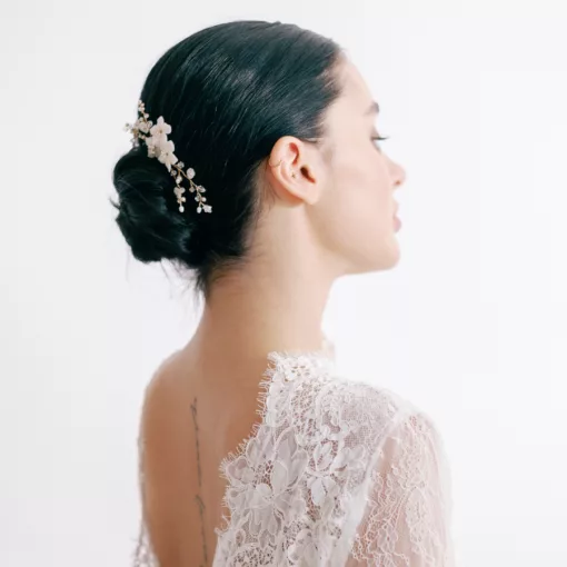 Clematis Wedding Hairpin. A woman looks away from the camera. She has dark hair, in a neat bun, and a floral bridal hair pin decorating the hair. She wears a lace wedding dress.
