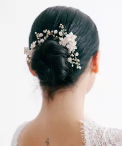 A woman looks away from the camera. She has dark hair, in a neat bun, and a freshwater pearl and crystal flower hair pin decorating the hair. She wears a lace wedding dress.