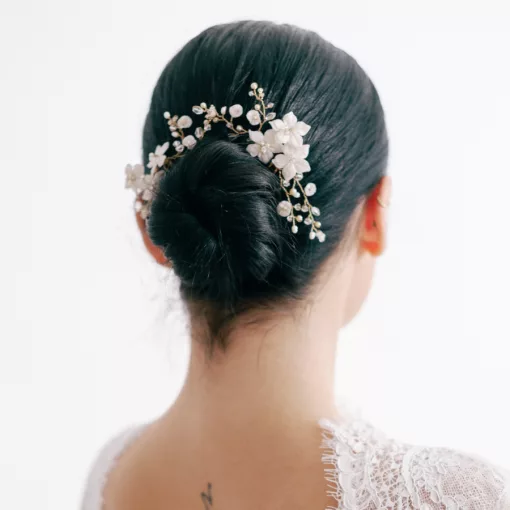 A woman looks away from the camera. She has dark hair, in a neat bun, and a freshwater pearl and crystal flower hair pin decorating the hair. She wears a lace wedding dress.