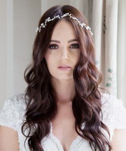 Bride in a bridal suite looking at the camera. She has long dark wavy hair with a Romantic whimsical bridal hair vine decorating it.