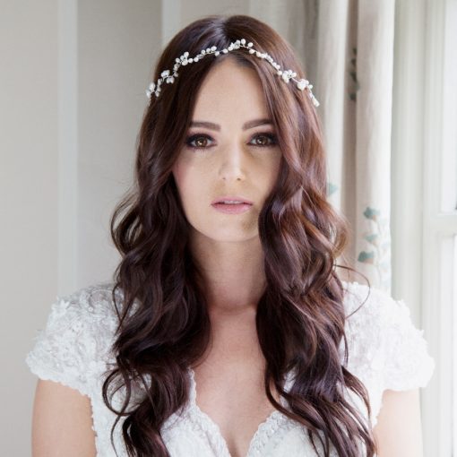 Bride in a bridal suite looking at the camera. She has long dark wavy hair with a Romantic whimsical bridal hair vine decorating it.
