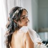 Bride wearing a bridal gown with large tulle bow at the shoulders. She has long curly dark hair and wears a Statement floral pearl bridal hair vine. Behind her are curtains to a large window.
