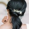 Image of woman with dark hair in a low pony tail wearing modern minimalist leaf wedding hair pins