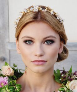 Dancing Bee Bridal Tiara. Bride wearing flower crown looking at the camera with blonde hair and blue eyes, with a floral wreath around her ne.ck