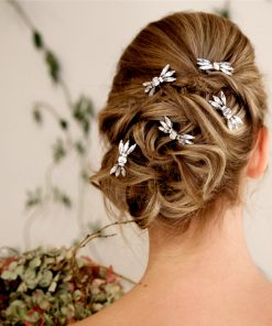 Bride looking away from the camera, holding a hydrangea bouquet, Her blonde hair is up in a messy curled updo and decorated with art deco diamante wedding hair pins