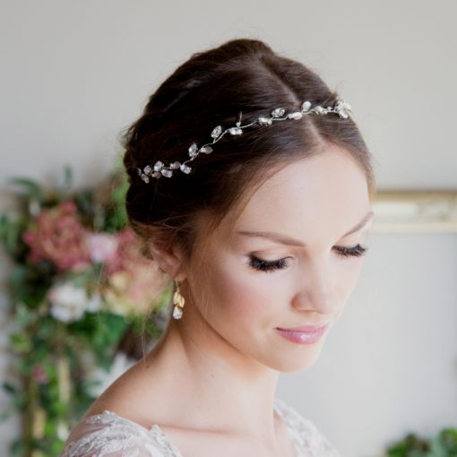 Bride looking down with her lace gown on and Botanical relaxed wedding hair vine in her dark hair that is styled in a neat bun. In the background is an ornate antique gold picture frame decorated with hydrangea flowers.