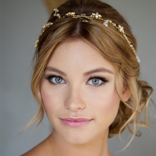 woman with blonde hair looking directly at the camera, with her hair in a low messy bun, wearing a celestial bridal halo hair vine