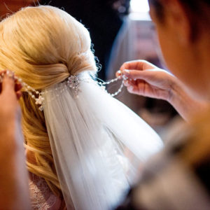 Bride is having a bridal hair chain inserted in to her hair above her veil by a hair stylist