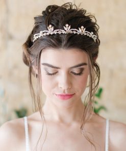 Bride looking down, wearing a strapped bridal gown. Her hair is up and she wears a Crystal Pearl handmade wedding tiara. In the background is a stone wall.