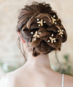 bride stood with her back to the camera. Her gown features straps. You can only see her shoulders. She faces a stone wall in a barn. Her hair is up in a curly messy updo with modern celestial starburst hair pins decorating it.