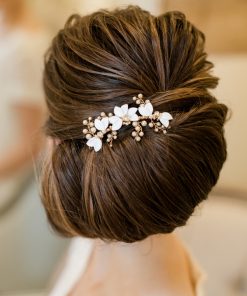 Bride looking away. She has dark hair in a neat large chignon decorated with a Small pearl and leaf wedding headpiece. In the background there is a cushion, and chair.