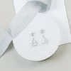 decadent teardrop diamante silver earrings set on a round white platform with silk blue ribbon and wedding invitation in the background.