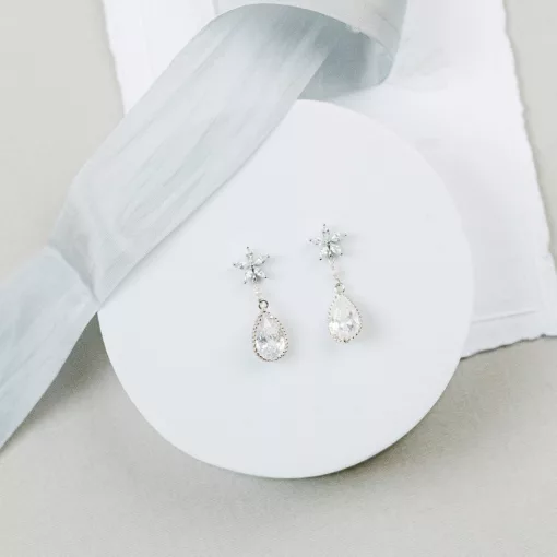 Diamante pearl drop Earrings set on a round white platform with silk blue ribbon and wedding invitation in the background.