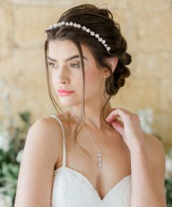 Woman stood with ivory wedding dress with straps, wearing a simple pearl wedding alice band with dark brown hair in a low braided updo.