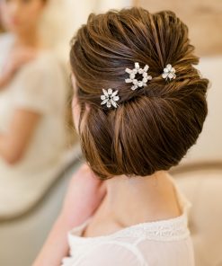 Bride looking away into a mirror in a bridal suite. She has her hair up in a stylish and neat chignon and wears Diamante jewelled hair pins