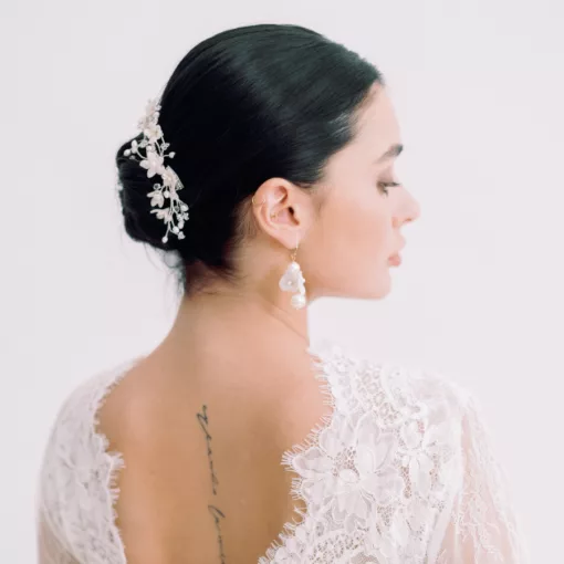 Rambling Rose Bridal Hairvine. A woman looks away from the camera. She has dark hair, in a neat bun, and a floral bridal hair vine decorating the hair. She wears a lace wedding dress.