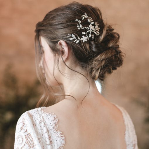 Bride in a barn with stone wall behind. She looks away, showing her hair in a low undone bun wearing a Small hair up wedding hair vine. Her gown has a low back and is covered in lace.