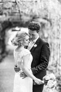 Bride and groom in black and white embracing in front of a floral arch