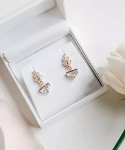 Gold diamante art deco style earrings in a jewellery box with blush silk ribbon in the background and a white rose.