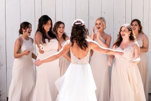Bride is greeting all her happy bridesmaids, with her arms out to embrace them.