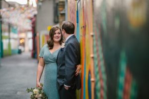 Bride in a teal wedding dress with her groom stood against a colourful city wall landscape