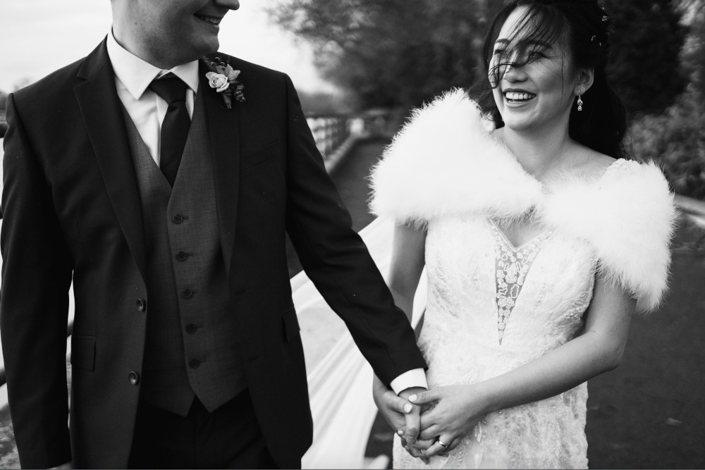 Bride and groom close up holding hands. The groom wears a blue suit and the bride is wearing a feather bolero.