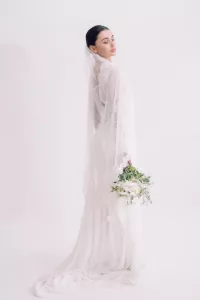 Bride wearing veil and wedding dress holding a white and green bridal bouquet against a white background