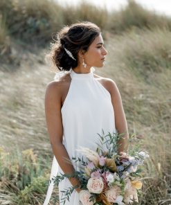 Beach scene with bride looking out to sea, holding a bouquet of flowers