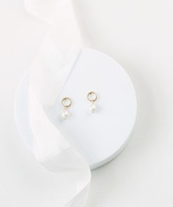 Contemporary circle stud pearl drop earrings on small white round platform with ivory silk ribbon and ivory fabric background