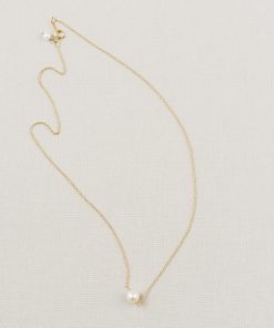delicate classic freshwater pearl bridal pendant in gold sat on a beige background.