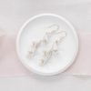 Small cream dish with bridal flower and pearl drop earrings laying on top. Underneath the dish is a beige fabric and blush pink silk ribbon