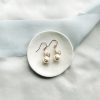 Image of large Swarovski pearl drop bridal earrings on small ivory dish, on a cream fabric background with blue ribbon