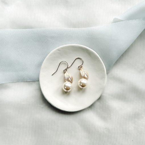 Image of large Swarovski pearl drop bridal earrings on small ivory dish, on a cream fabric background with blue ribbon