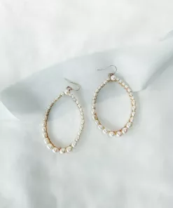 Blythe Pearl Hoop Earrings. Image shows white fabric background with blue silk ribbon and large pearl hoop earrings in gold
