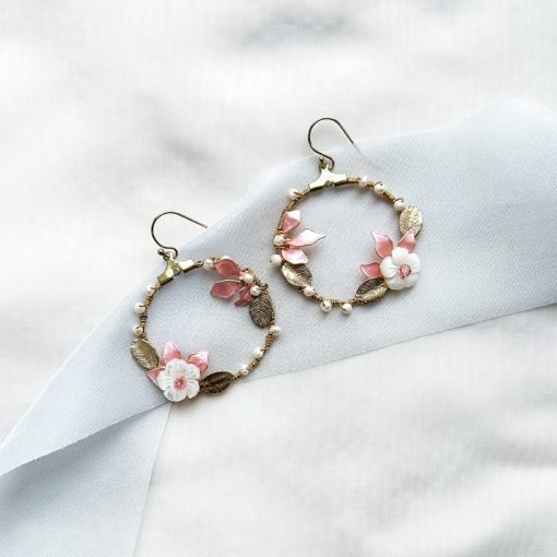 gold hoop earrings with leaves and flowers laying flat on ivory material with blue ribbon