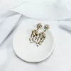 Image shows white fabric background with blue silk ribbon draped across, with small clay bowl on top with Victorian style crystal and pearl chandelier earrings