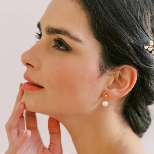 Vivienne Pearl Drop Earrings - woman with hand on her face looking to the side wearing gold stud pearl drop earrings.