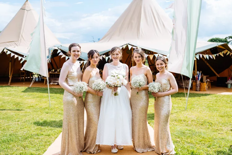 Is it normal to feel anxious planning a wedding? Large tipi in background with bride standing in front holding flowers with her 4 bridesmaids wearing gold dresses