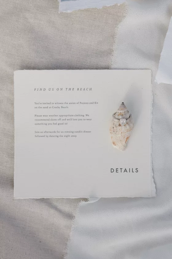 Is it normal to feel anxious planning a wedding? Beach wedding invitation with shell placed on top with a diamond engagement ring on a table cloth
