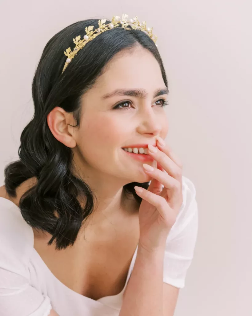 Wedding tiaras and how to wear them. Woman looking away from the camera wearing a tiara and holding her hand to her mouth as she smiles.