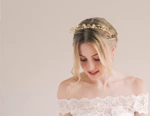 Wedding tiaras and how to wear them. Woman looking down with tiara on her head, and wearing a lace wedding gown off the shoulder. The background is plain.