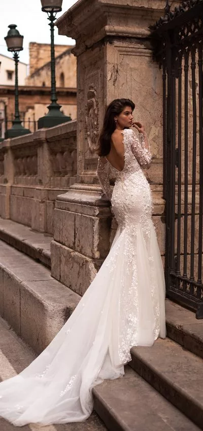 Bride standing on stone steps next to a black iron gate. She wears a white bridal gown