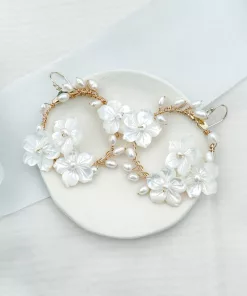 Large delicate handmade floral pearl hoop wedding earrings set on a cream dish, overlaying an ivory fabric background with light blue silk ribbon.
