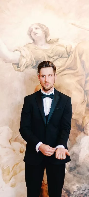 Groom in black tuxedo standing in front of a renaissance mural