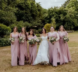 bride standing with bridesmaids in gardens, all holding bouquets of flowers.
