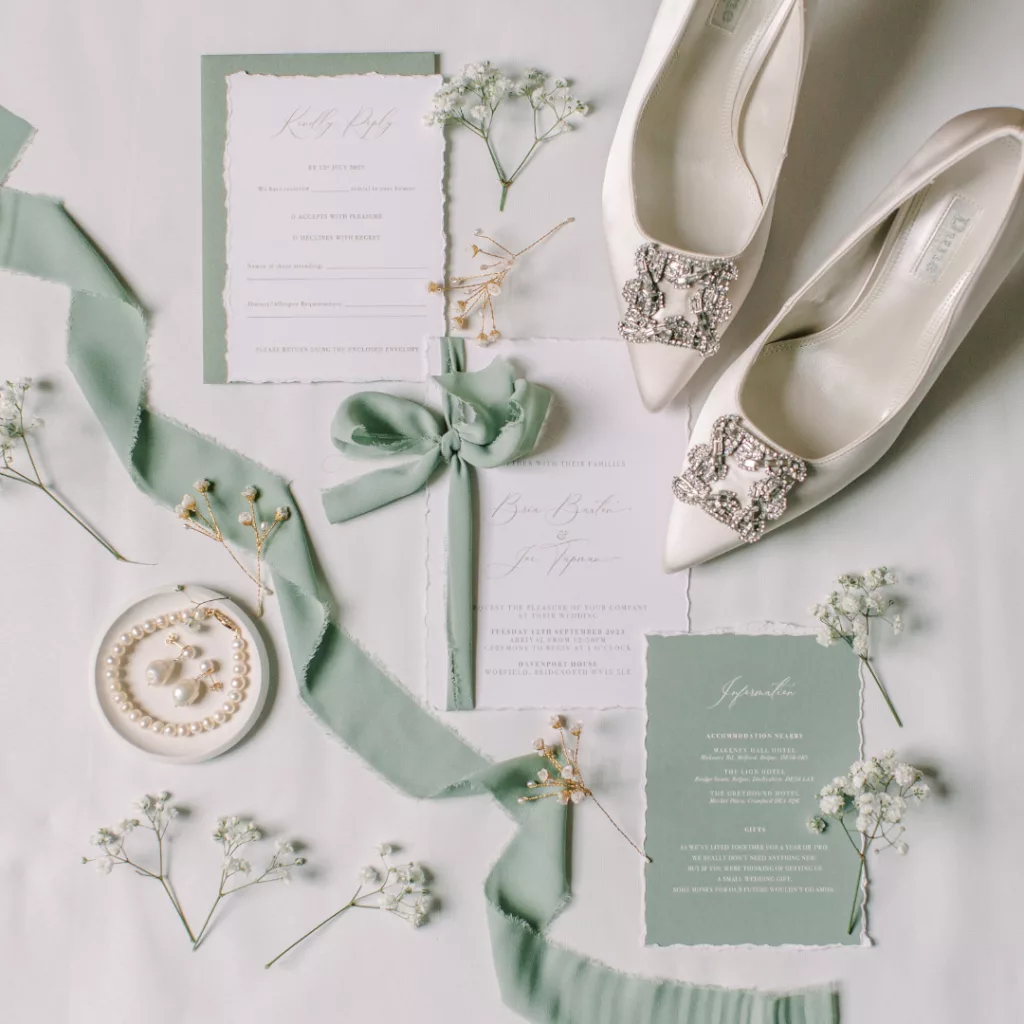 Shades of green wedding inspiration with gypsophila. Image shows a flat lay of green ribbons, and green and white wedding stationery, with jewellery laid out gypsophila and ivory bridal shoes